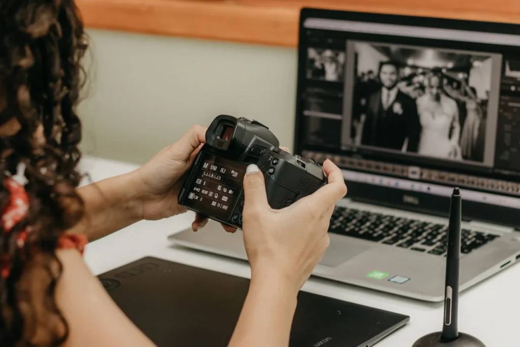 Photographer holding a camera, editing photos on a laptop using Adobe Lightroom with a stylus and tablet.